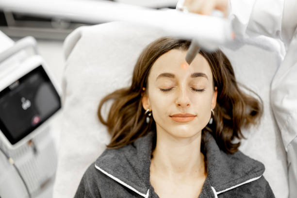 Cosmetologist doing laser facelifting procedure to woman in beauty clinic. Anti-age, non-invasive, non-surgical laser facelift for natural-looking results concept. Close up. View from above.